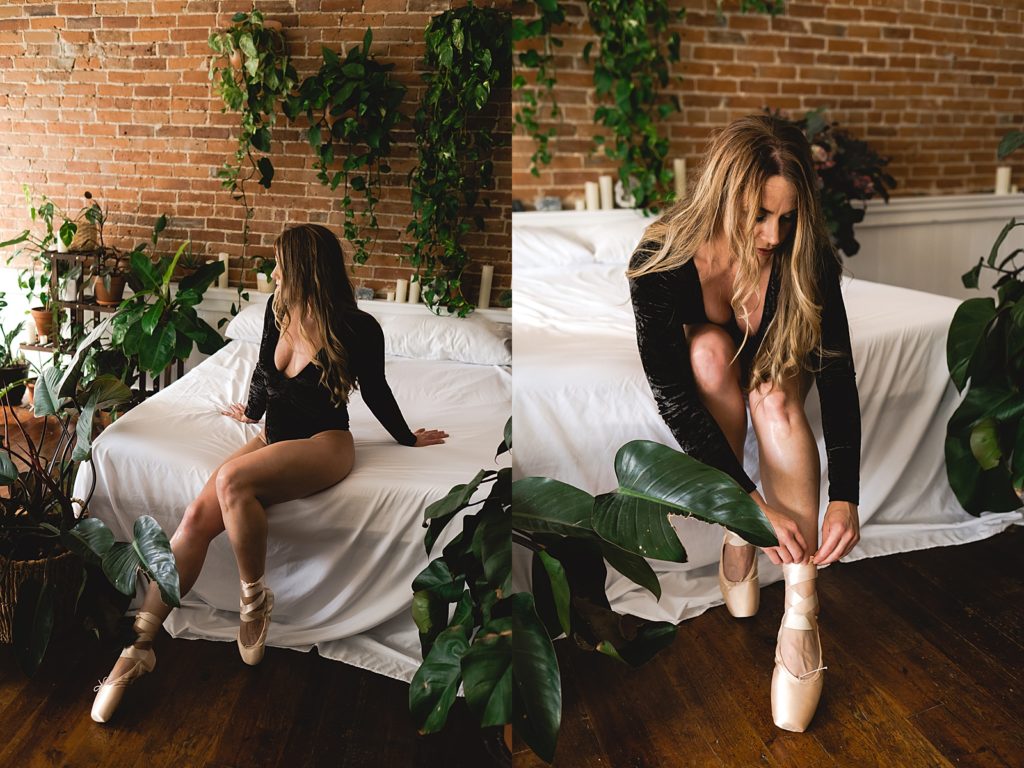 Woman in black lingerie and ballet shoes sitting on a bed surrounded by plants for boudoir shoot.