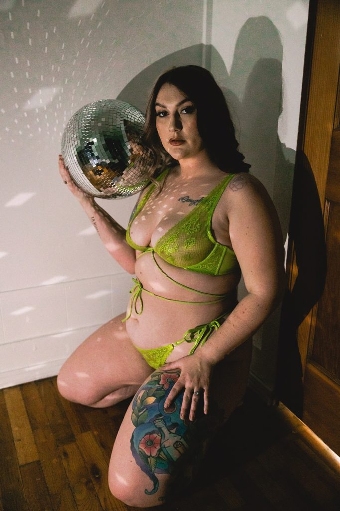 Woman in lime green lingerie holding a disco ball for her boudoir session with WMNKND Boudoir in Kansas. 