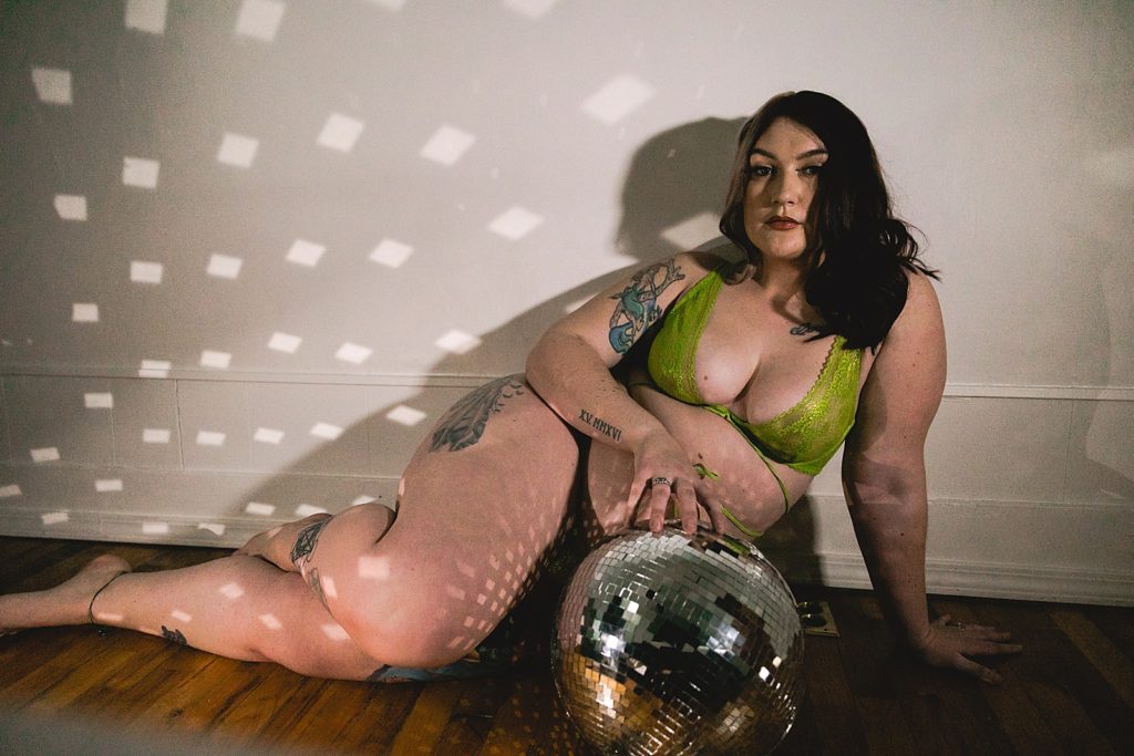 Woman in a lime green two piece lingerie set holding a disco ball for her boudoir photo shoot.
