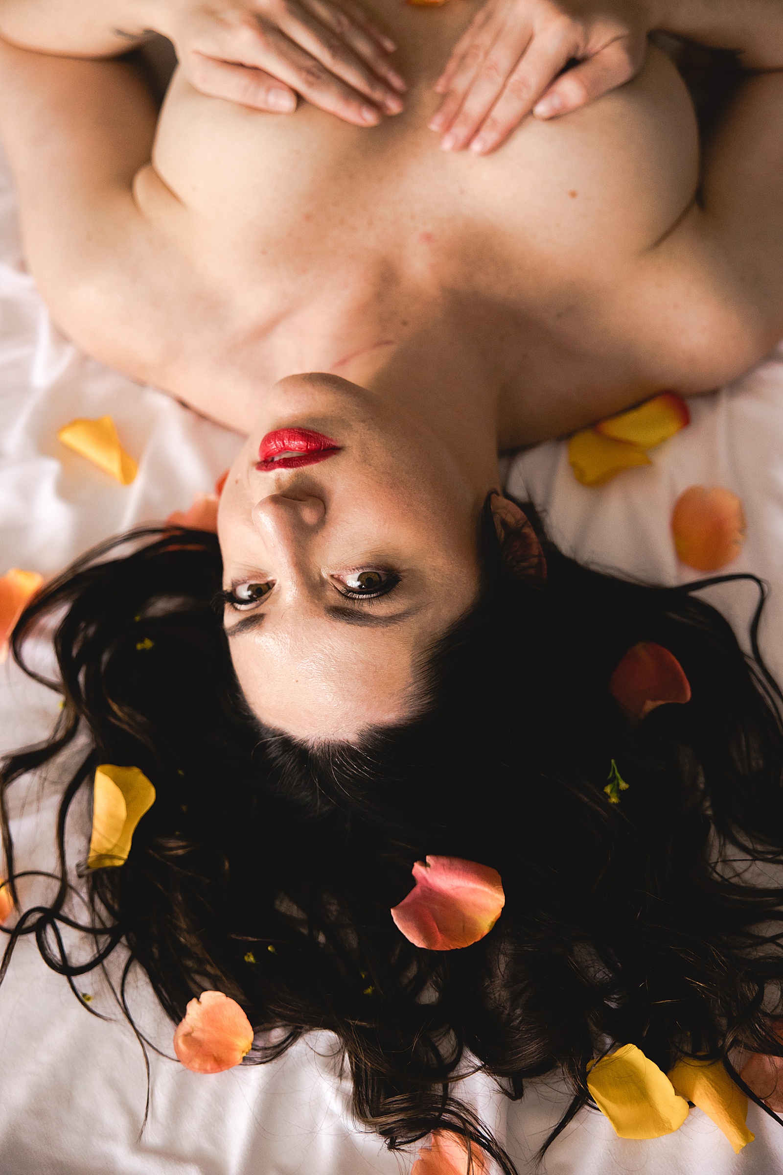 Nude woman lying on a bed with yellow flower petals all around