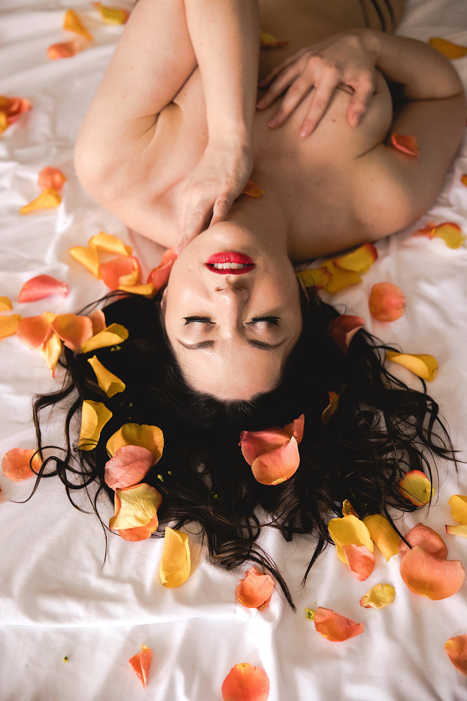 Topless woman on a bed with flower petals all around her 